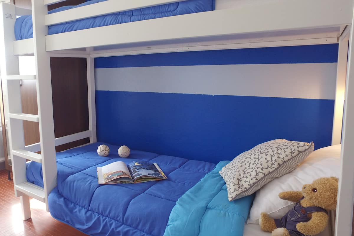 A bunk bed with a blue and white striped headboard, a teddy bear, and a book on the lower bunk.