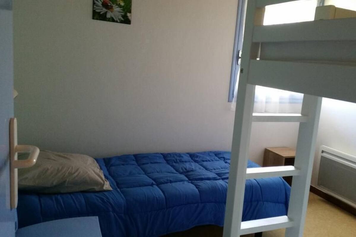 A bunk bed with a blue mattress, a pillow, a small bedside table, and a radiator.