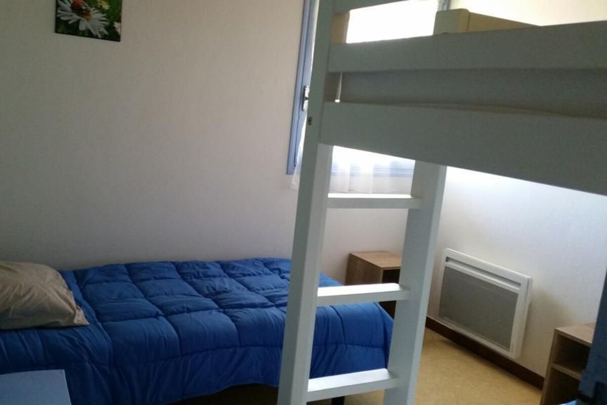 A bunk bed with a blue mattress, a pillow, a small bedside table, and a radiator.
