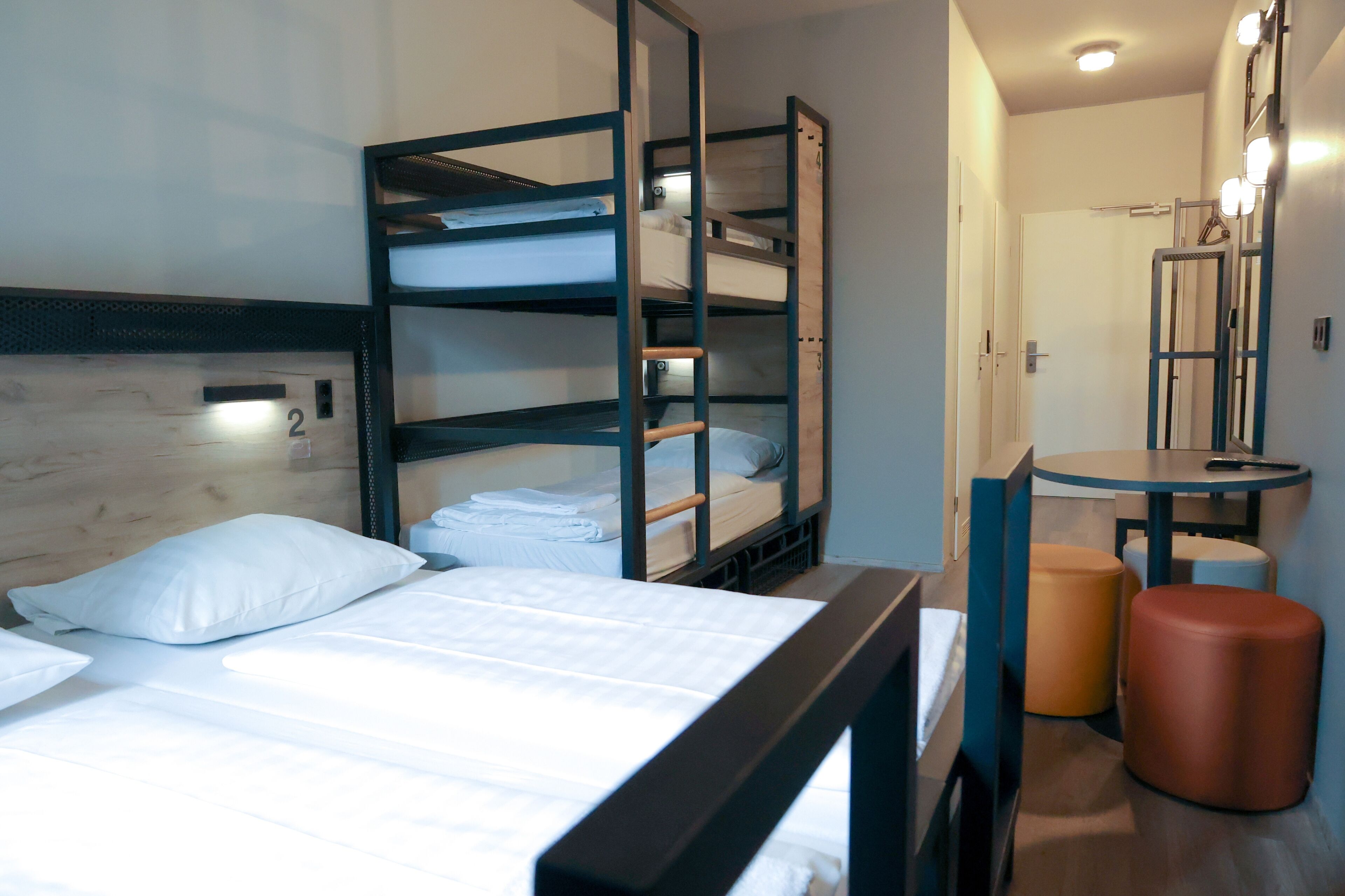 A bunk bed room with a wooden headboard, a small table with a mirror, and two stools.