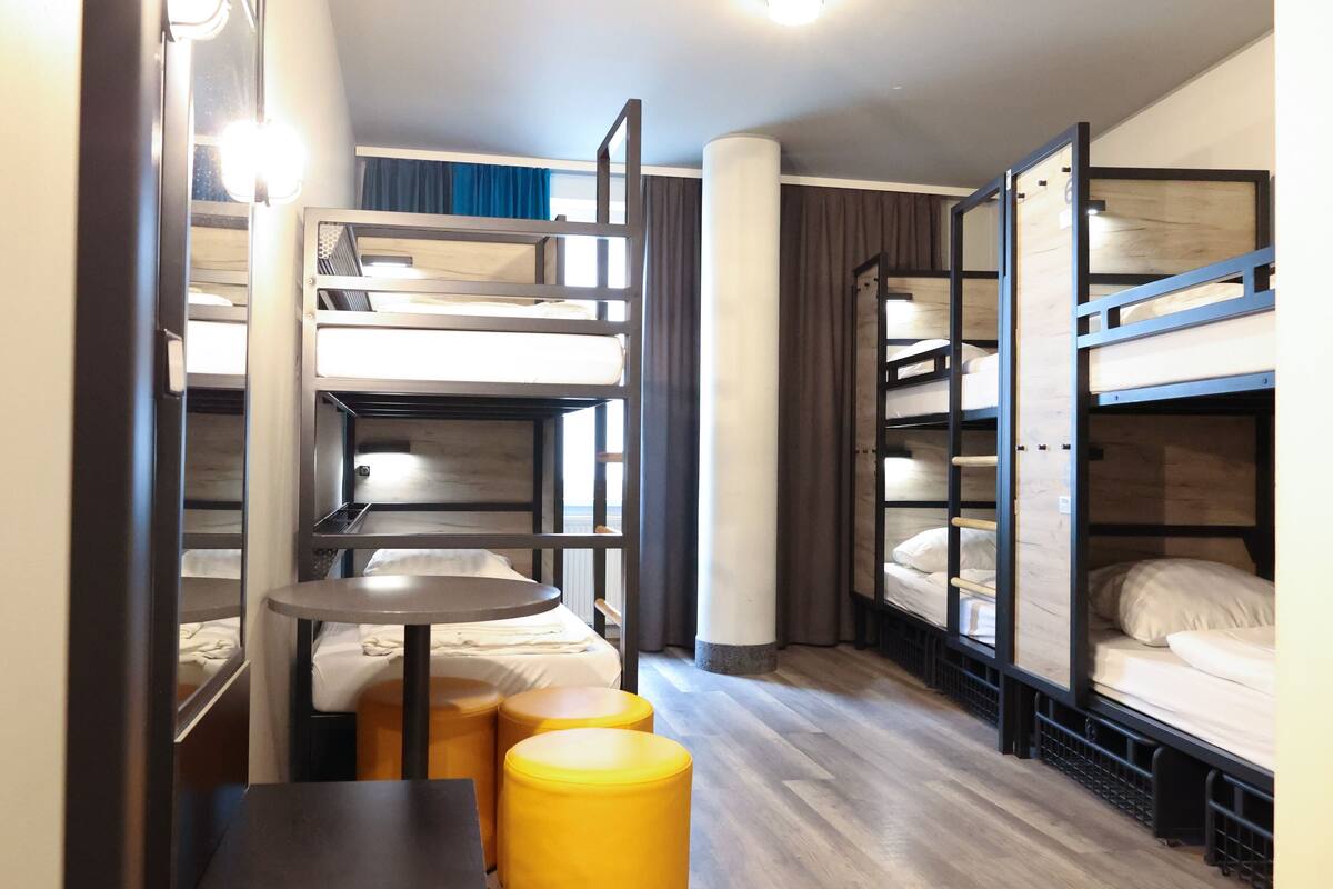 Habitación de hotel compacta con literas, una pequeña mesa redonda y dos otomanas amarillas.