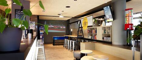 A modern cafe with a long counter, stools, and a seating area with round tables and chairs.