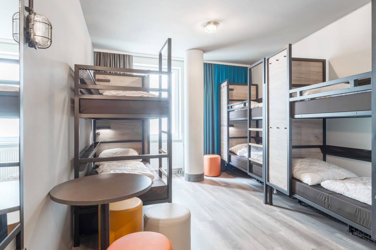 Una habitación de hotel moderna con literas, una mesa redonda y otomanas.