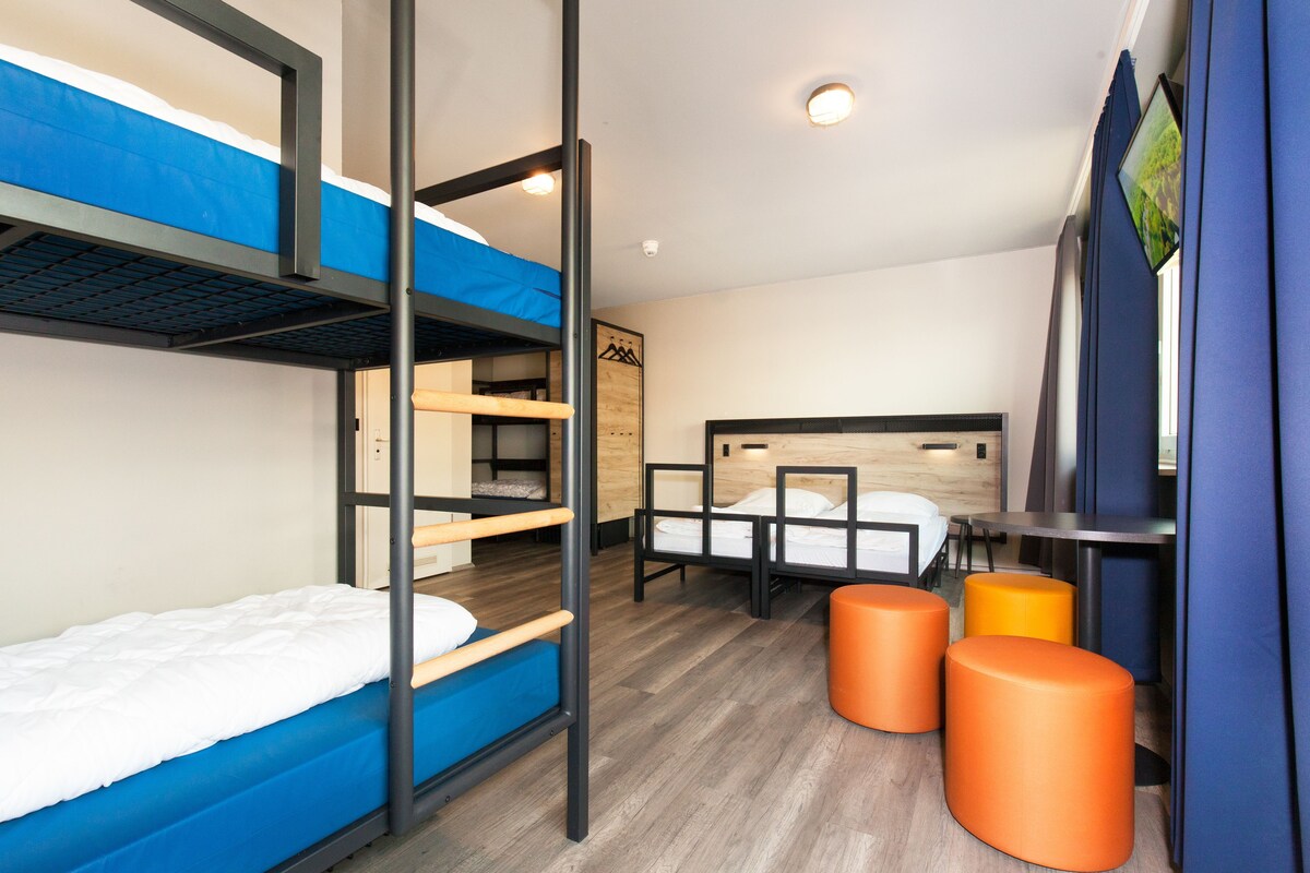 A bunk bed room with a wooden headboard, a desk, and orange stools.