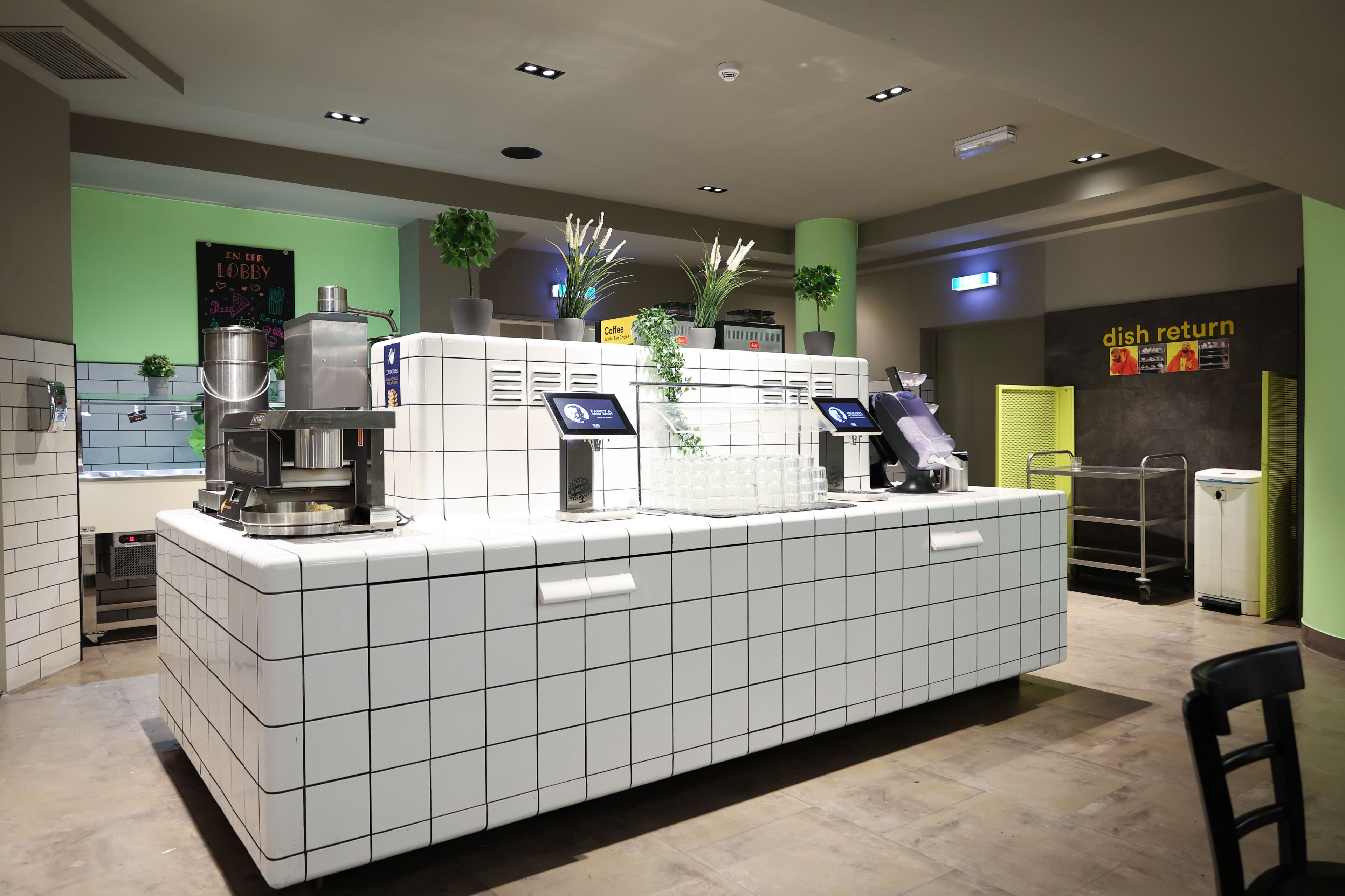 A modern coffee station with a self-service coffee machine, a digital menu board, and a sign indicating a dish return area.