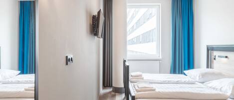 Habitación de hotel con dos camas, televisión, ventana con cortinas y suelo de madera.