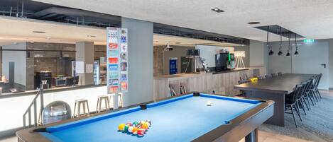 Une table de billard recouverte d’un drap bleu et dotée d’une boule blanche, entourée de chaises.