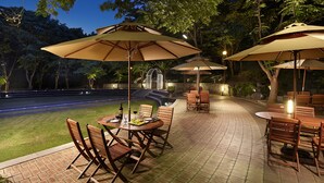 An outdoor patio area with tables and chairs under umbrellas, surrounded by trees and a pool. - The K-Hotel Seoul (Seoul)