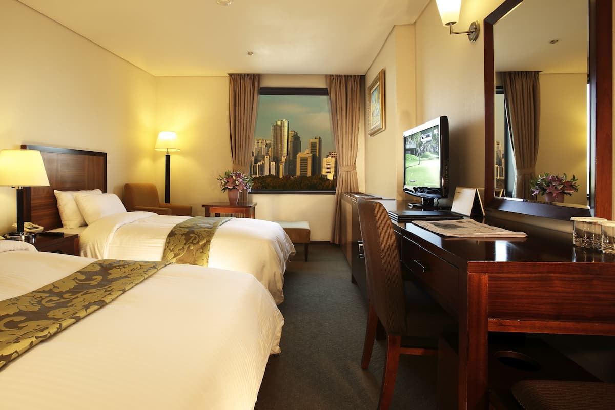 Habitación de hotel con dos camas, un escritorio, una silla, un televisor y vistas a la ciudad.