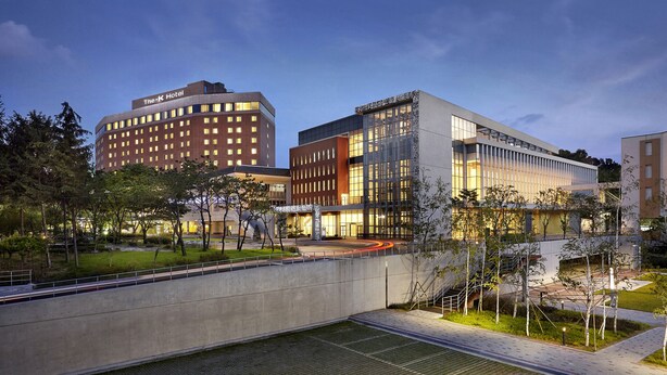 A modern hotel with a prominent 'The K Hotel' sign, a landscaped courtyard, and a pedestrian bridge. - The K-Hotel Seoul (Seoul)