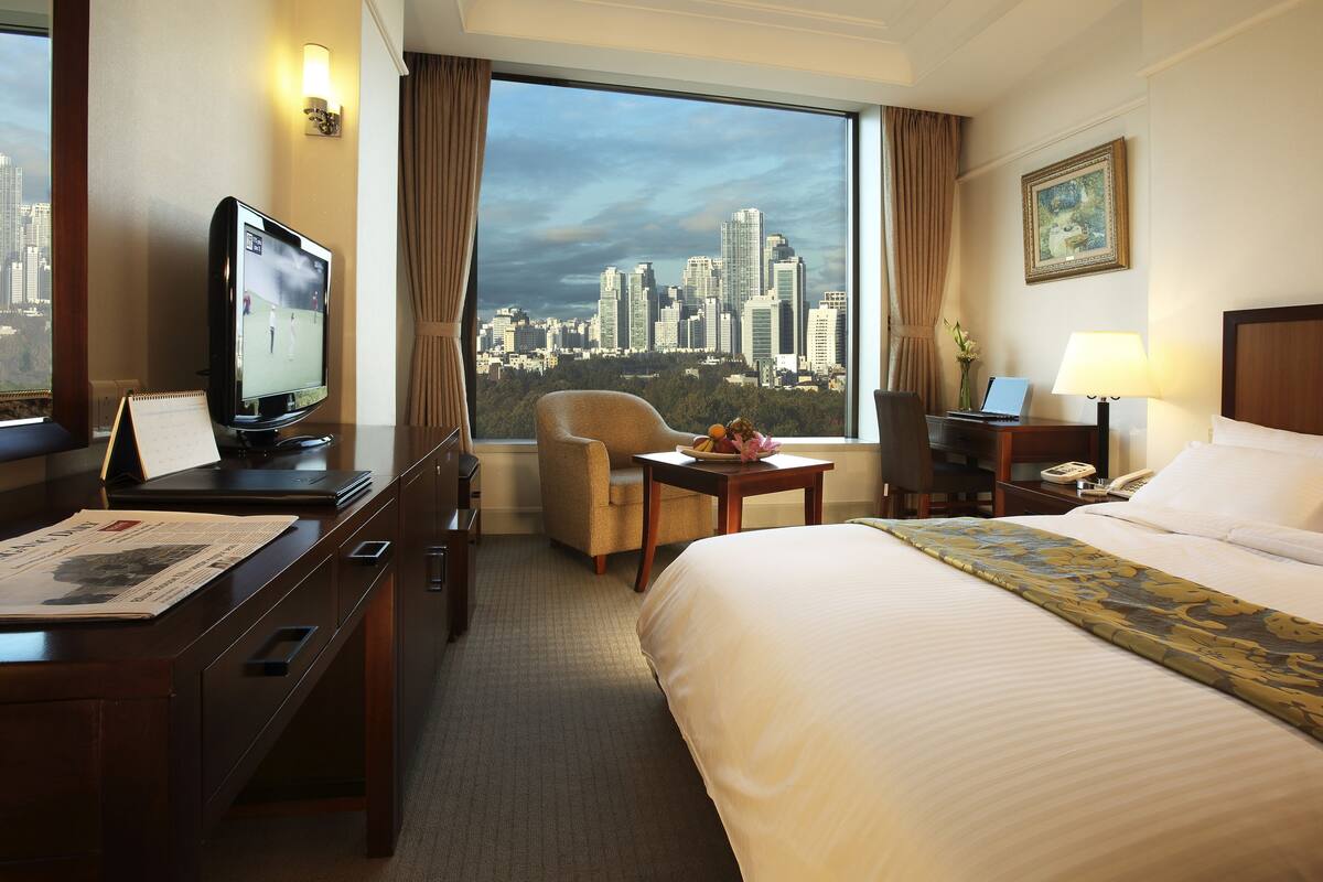 Habitación de hotel con cama, escritorio con computadora, silla, televisor y vista a la ciudad.