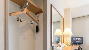 A hotel room with a wooden desk, two lamps, a television, a mirror, a coat rack, and a pair of slippers. - Ginza Capital Hotel Main (Tokyo)