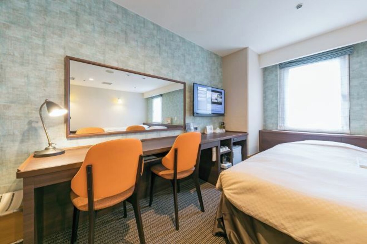 Ett hotellrum med en säng, ett skrivbord med två stolar, en tv och en stor spegel.