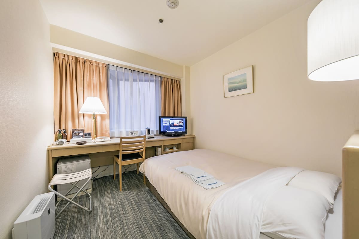 A hotel room with a bed, desk, chair, TV, and a window with curtains.
