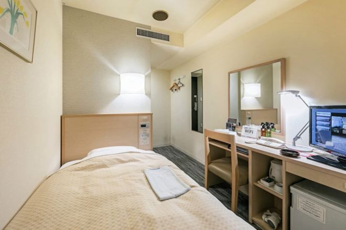 Ett hotellrum med en säng, ett skrivbord med en dator, en spegel och ett litet skåp.