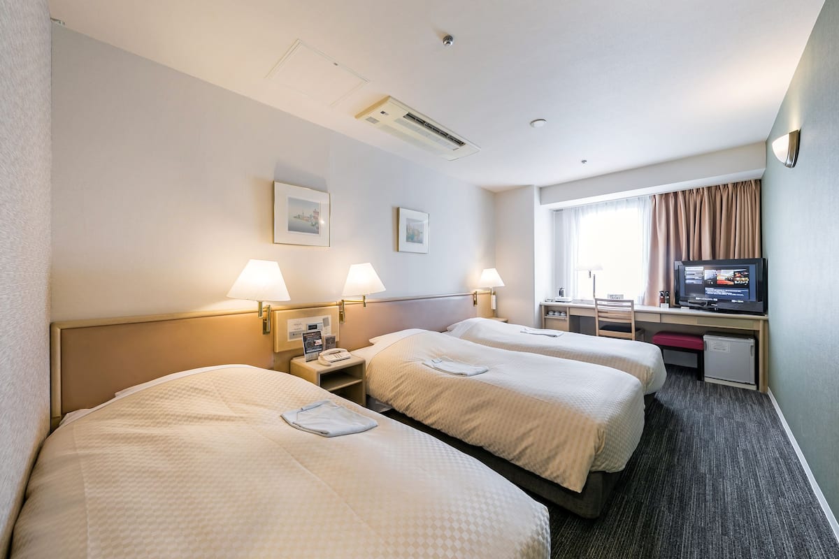 A hotel room with two beds, a desk with a television, and a window with curtains.
