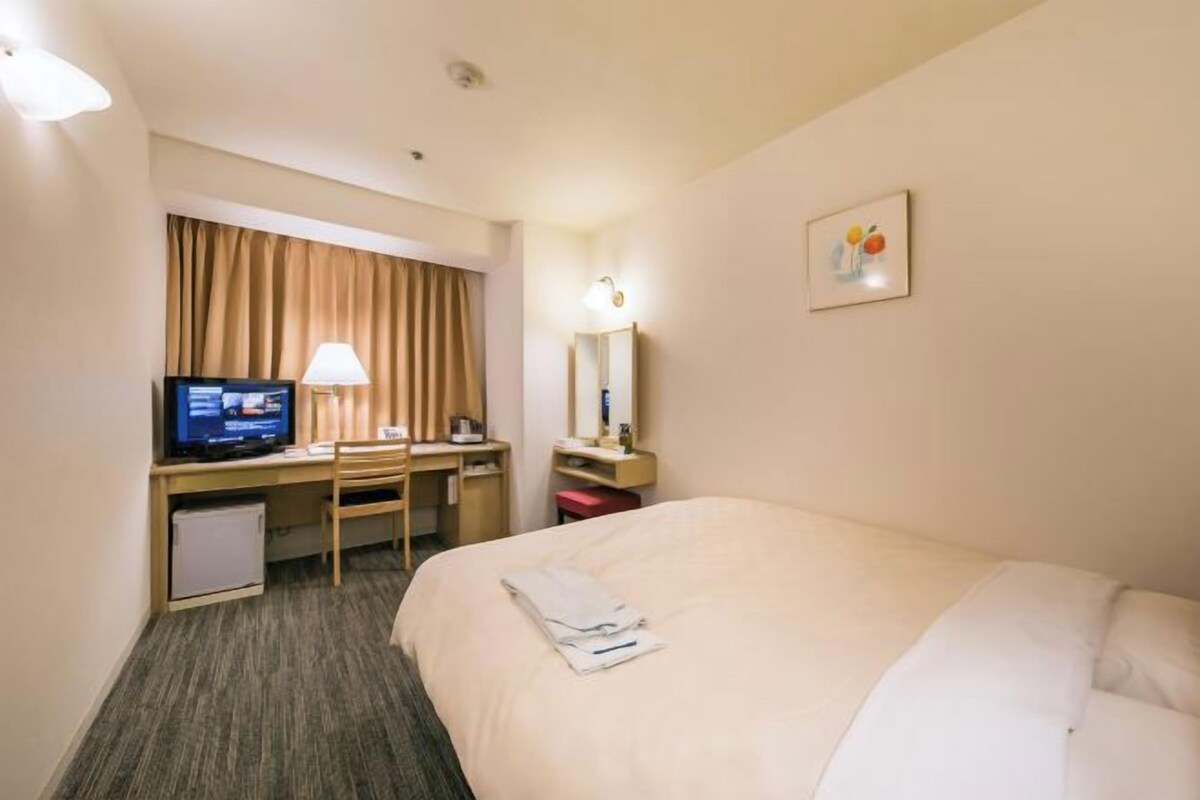 Una camera d'albergo con un letto, una scrivania con un computer, una televisione e un piccolo frigorifero.