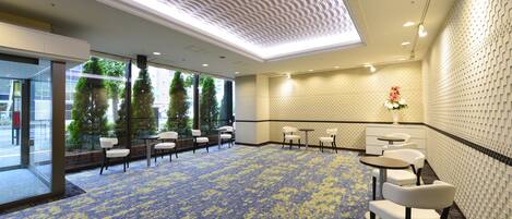 A spacious room with a patterned carpet, white chairs, and tables arranged for dining or meetings.