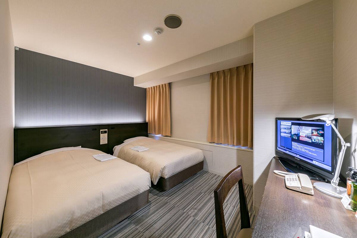 A hotel room with two beds, a desk with a computer and phone, and a television.