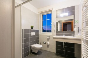 A modern bathroom with a toilet, a sink, a mirror, and a window. - Wine Wellness Hotel Amande (Hustopece)
