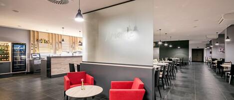 Un restaurante moderno con una zona de bar, asientos rojos y una pantalla grande que muestra el nombre del restaurante.