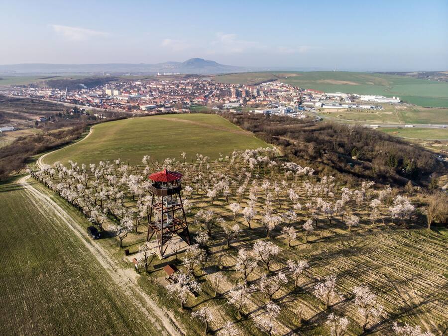 Vista aérea de un pueblo con un amplio campo abierto, una torre y un paisaje urbano distante.