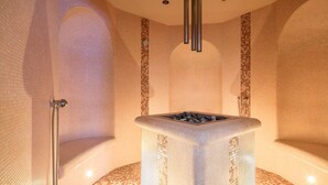 Un cuarto de spa con una bañera de hidromasaje de piedra, paredes enlosadas y un techo con una lámpara central.