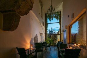 A cozy interior with a stone archway, a chandelier, and a view of a staircase leading to a balcony. - Wine Wellness Hotel Amande (Hustopece)