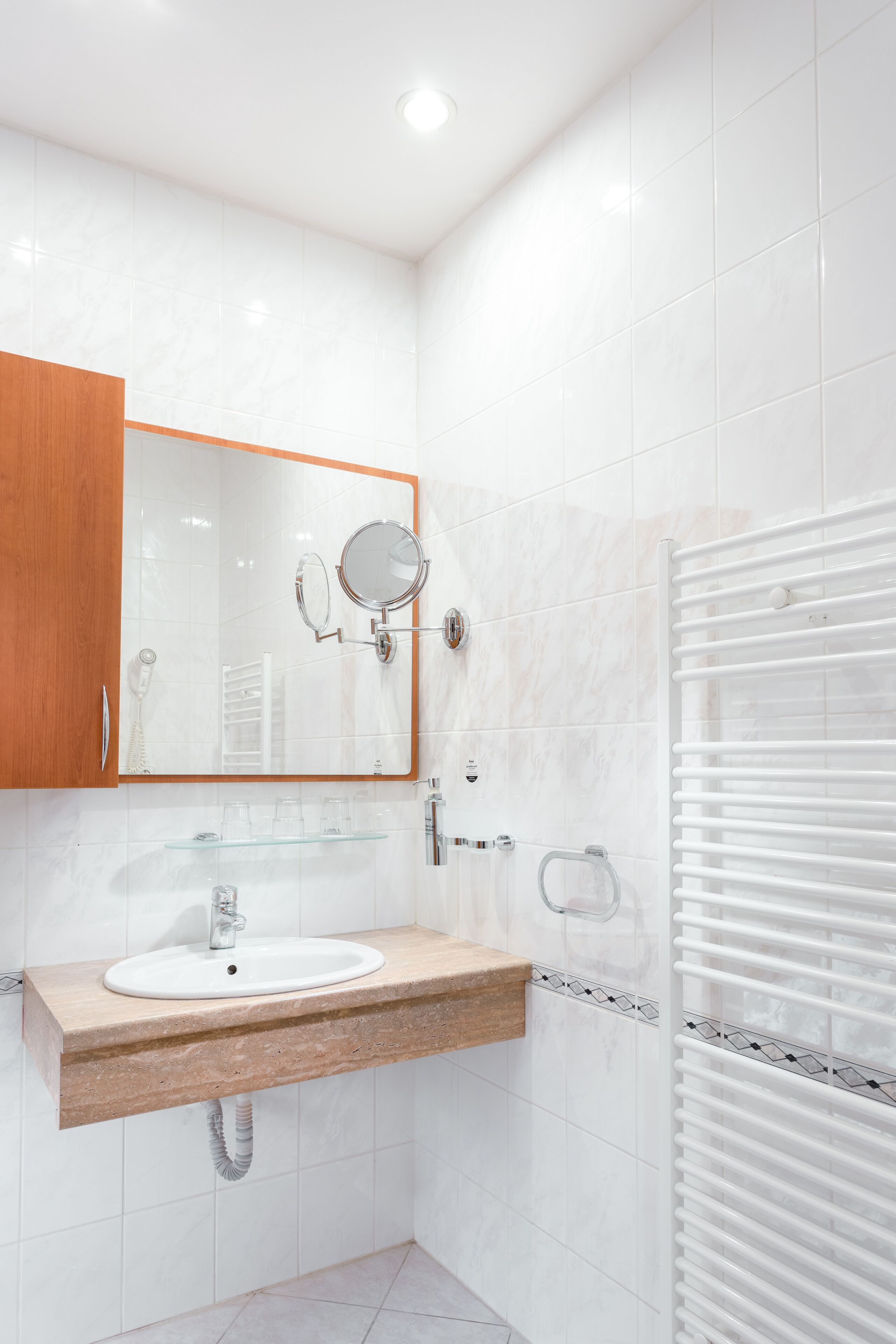 A modern bathroom with a white sink, wooden vanity, a large mirror, and a towel rack.