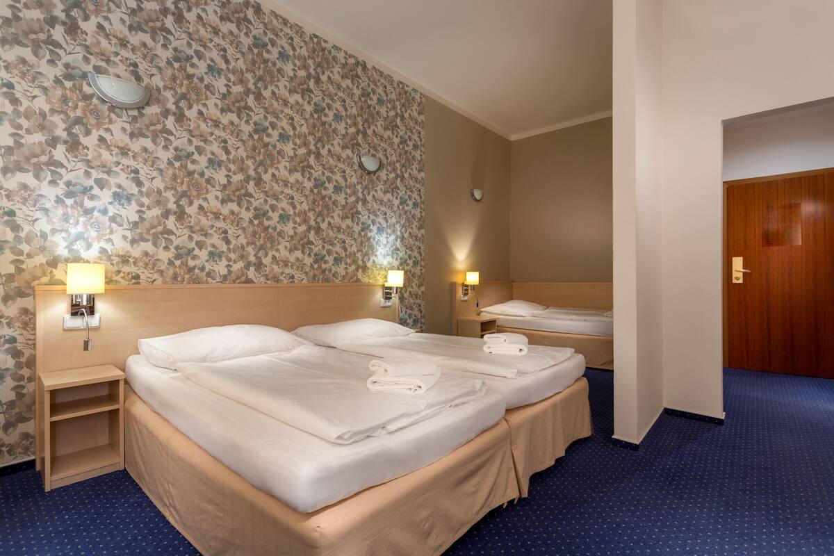 A hotel room with two beds, a wooden headboard, floral wallpaper, and a blue carpet.