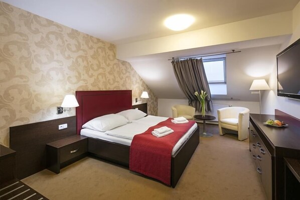 Habitación de hotel con una cama grande, televisión, escritorio con una bandeja de frutas, una silla y ventana con cortinas.
