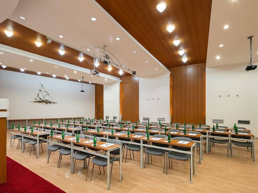 Un salón de conferencias con filas de mesas y sillas, equipado con proyectores e iluminación.
