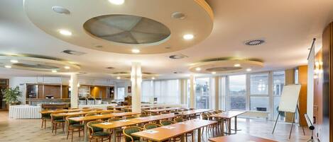 A spacious conference room with multiple tables and chairs, large windows, and a modern ceiling design.