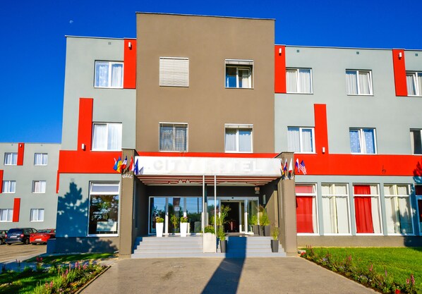 Un hotel moderno con fachada roja y gris, ventanas grandes y una entrada acogedora con escalones.