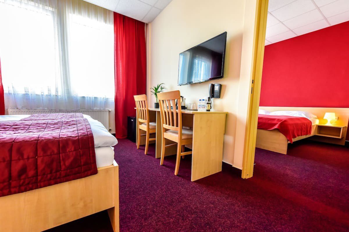 A hotel room with a bed, a desk with a chair, a television, and a second bed.