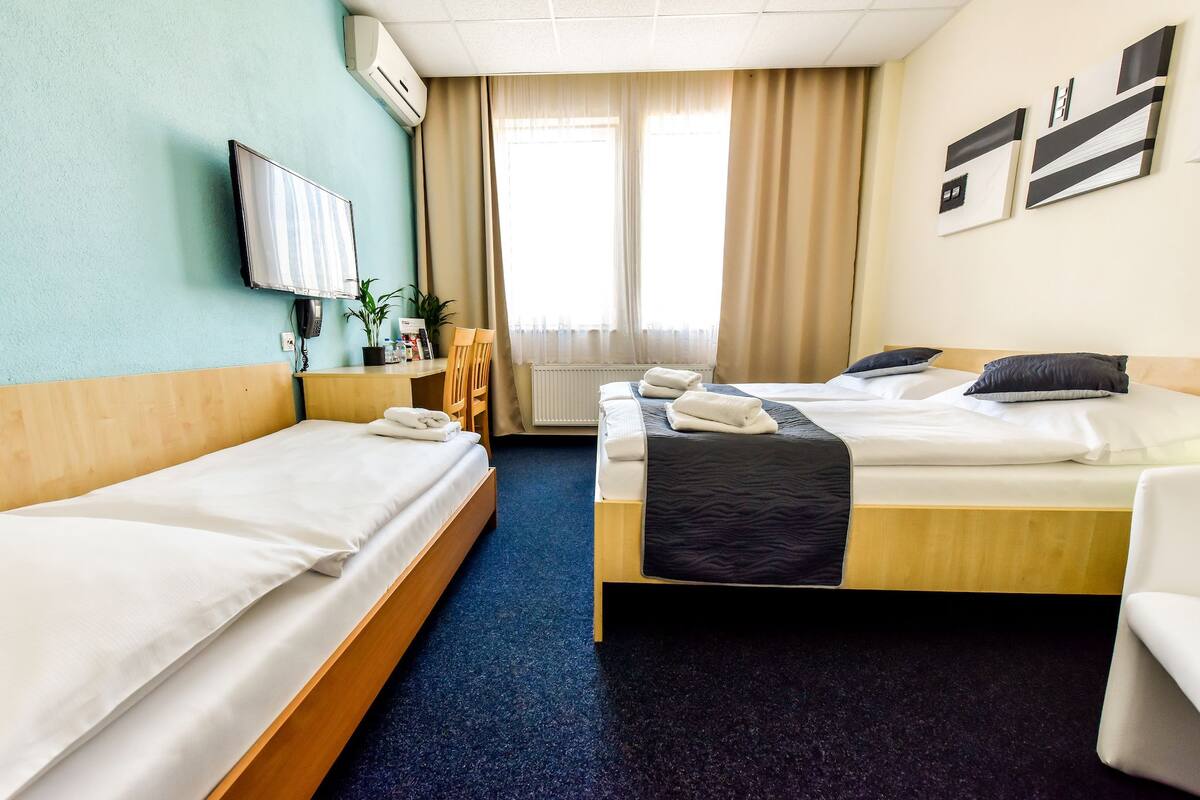 A hotel room with two single beds, a desk, a chair, a TV, and a window with curtains.