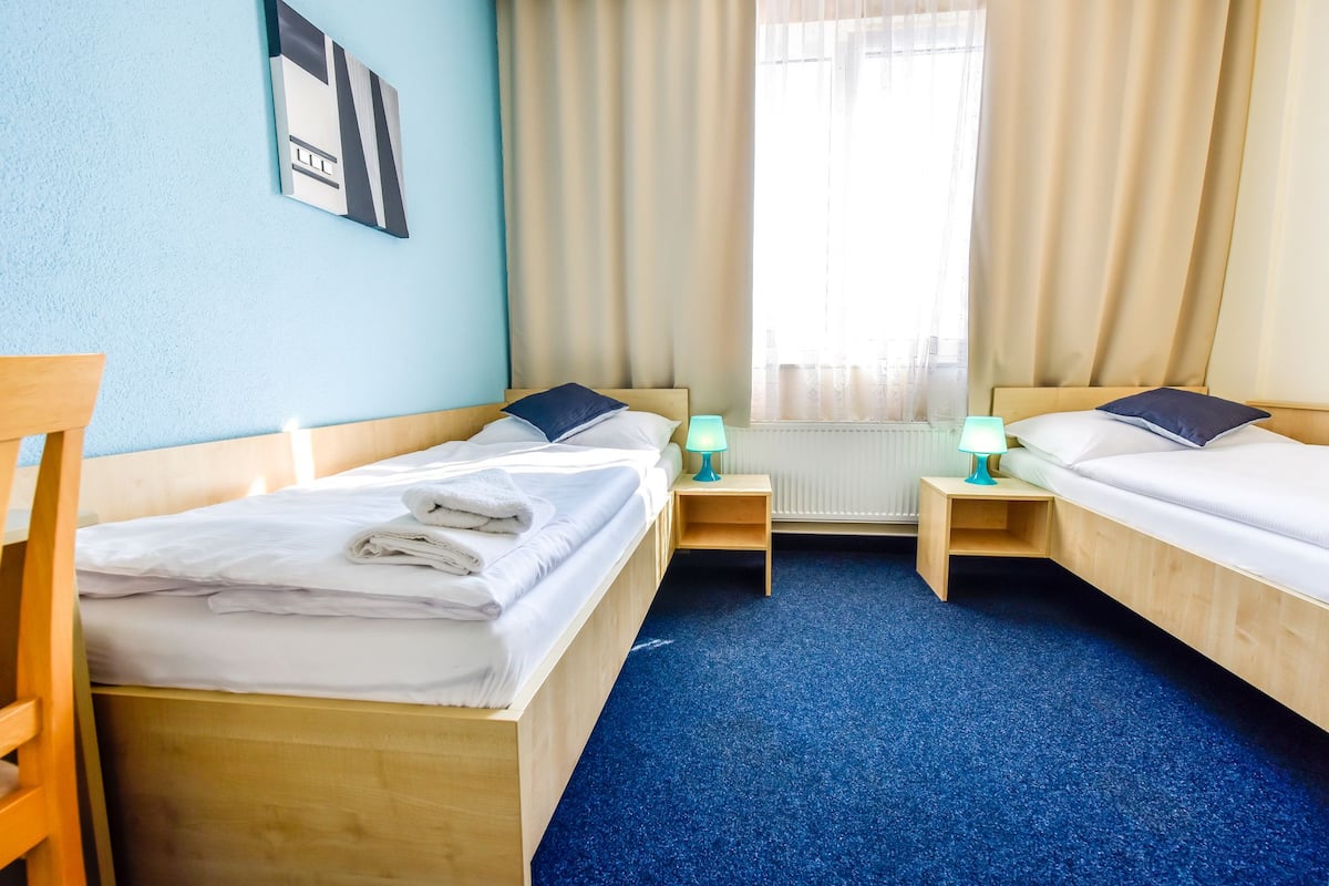 A hotel room with two beds, a wooden chair, a small table, and a window with curtains.