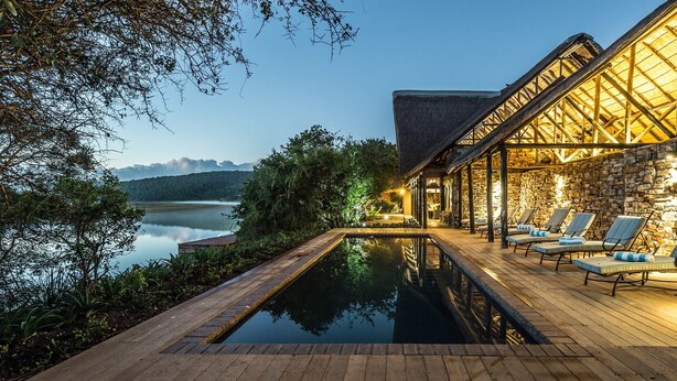 A poolside area with lounge chairs and a stone building with a wooden roof.