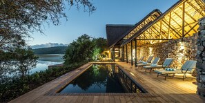 A poolside area with lounge chairs and a stone building with a wooden roof. - Kariega Game Reserve - River Lodge (Kenton on Sea)