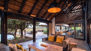 A spacious outdoor seating area with a wooden table, cushioned sofas, and a thatched roof structure.