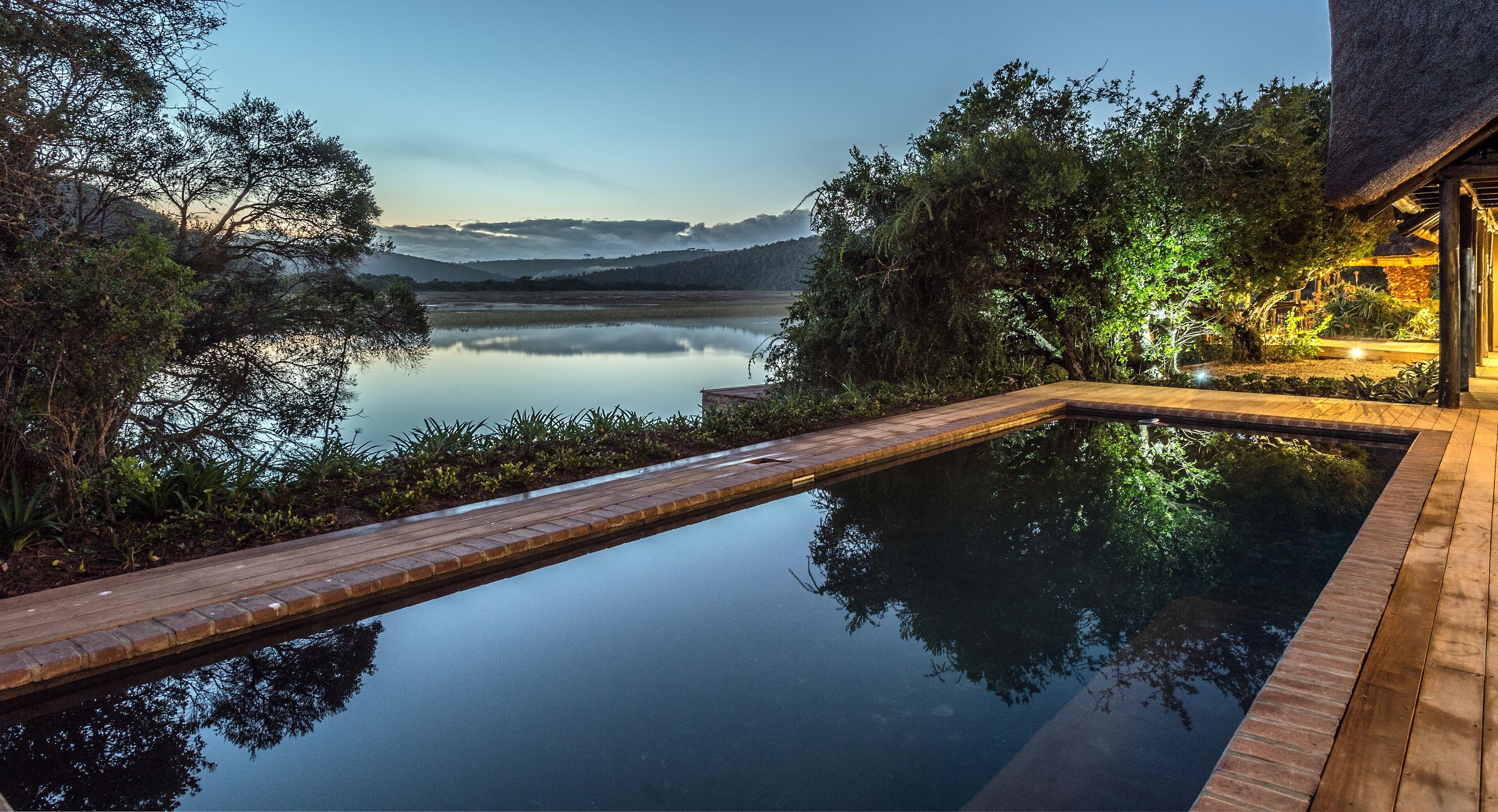 Tranquila zona de piscina al aire libre con un deck de madera, rodeada de exuberante vegetación y un paisaje montañoso.