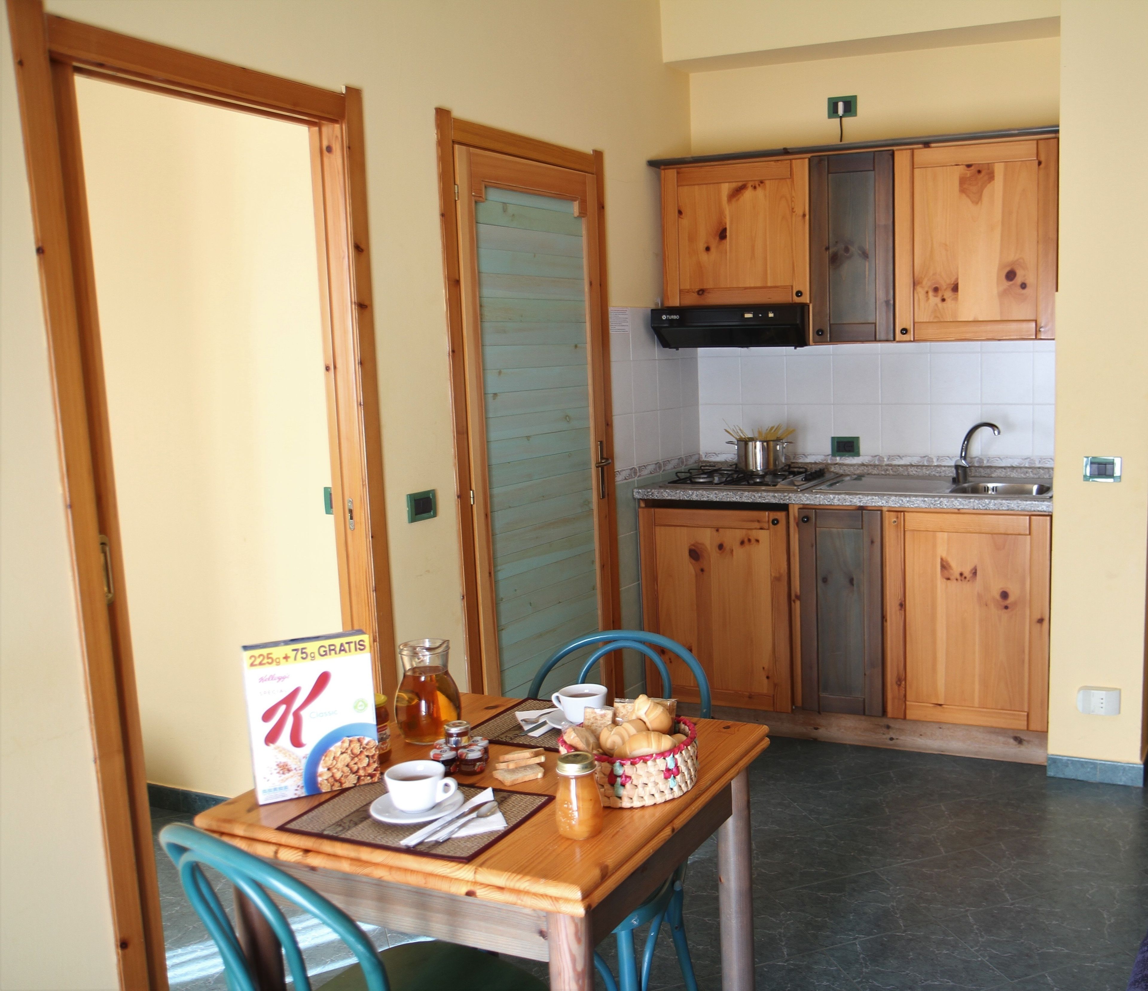 Una cocina pequeña con armarios de madera, un lavamanos y una mesa de comedor dispuesta para el desayuno.