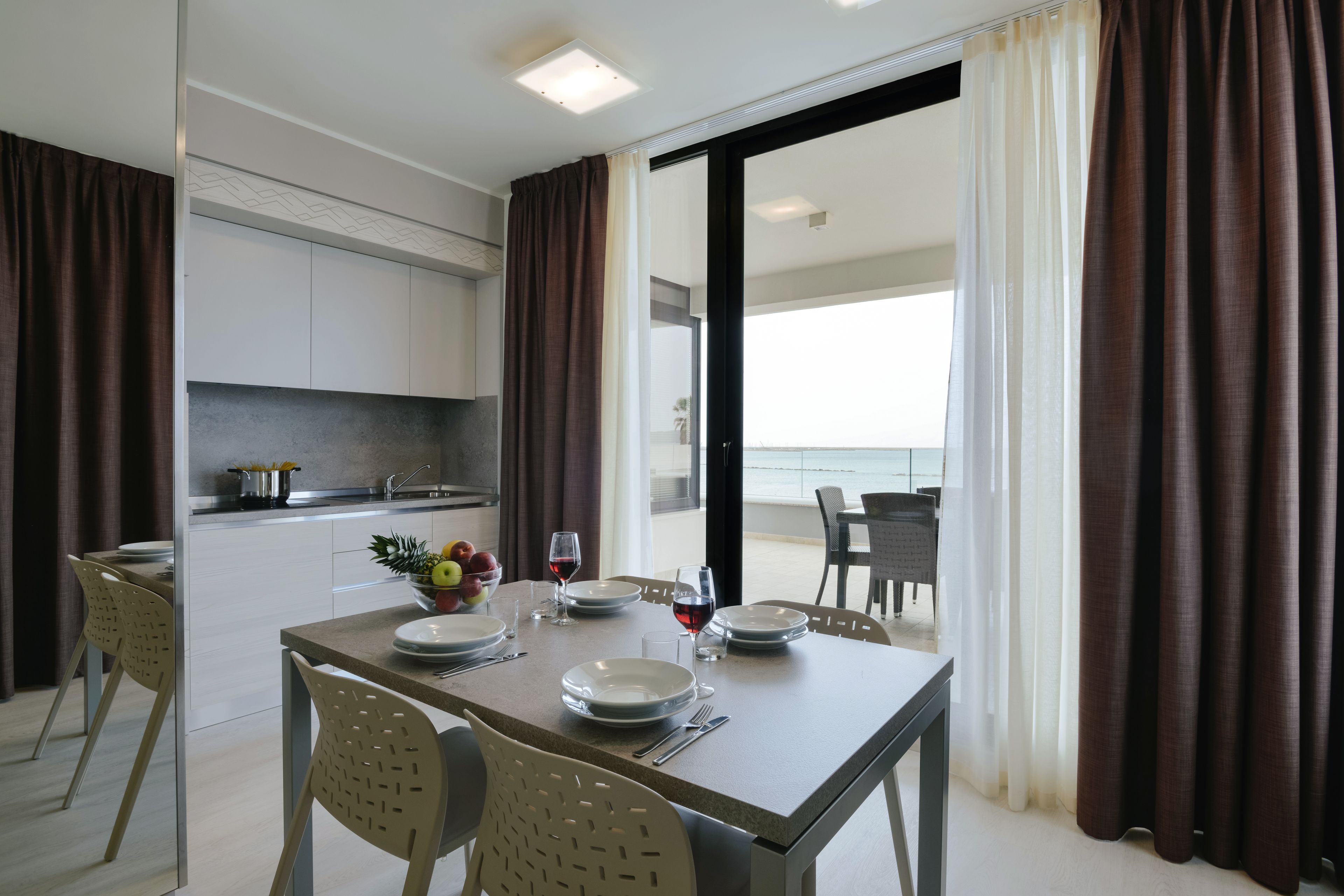 Una cucina moderna con mobili bianchi, un tavolo da pranzo apparecchiato per quattro e vista sul mare attraverso ampie finestre.