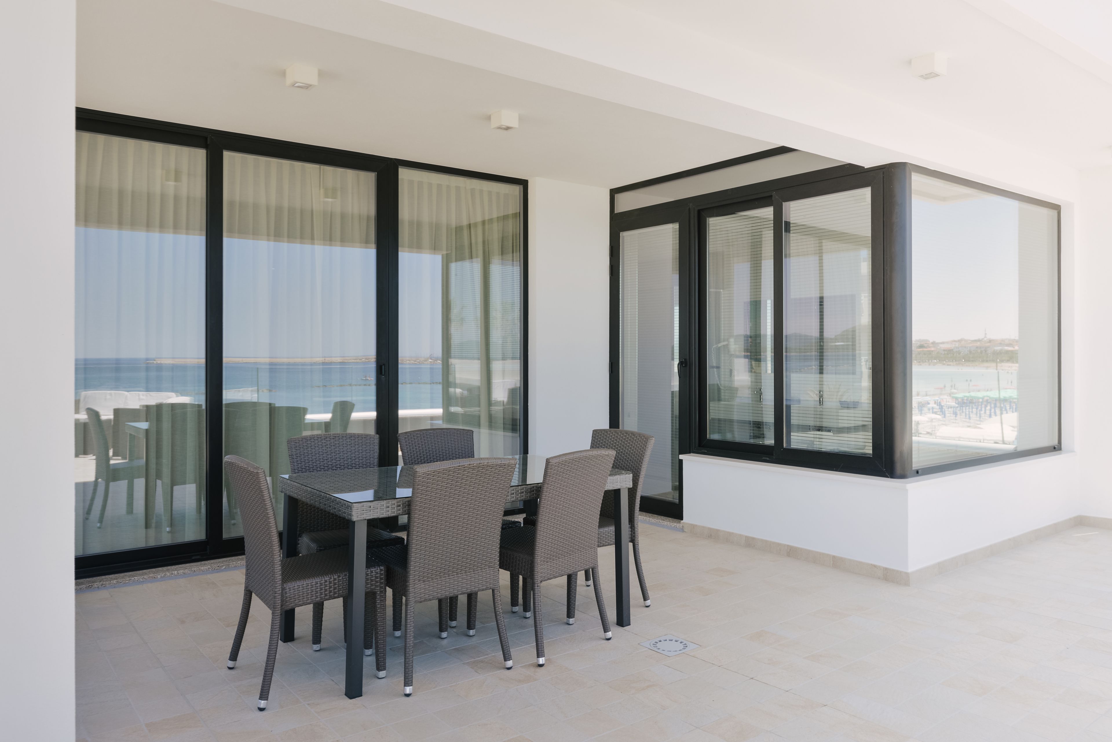 A balcony with a glass table and chairs, overlooking a cityscape.