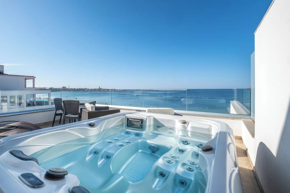 A hot tub on a balcony with a clear view of the sea and distant cityscape.