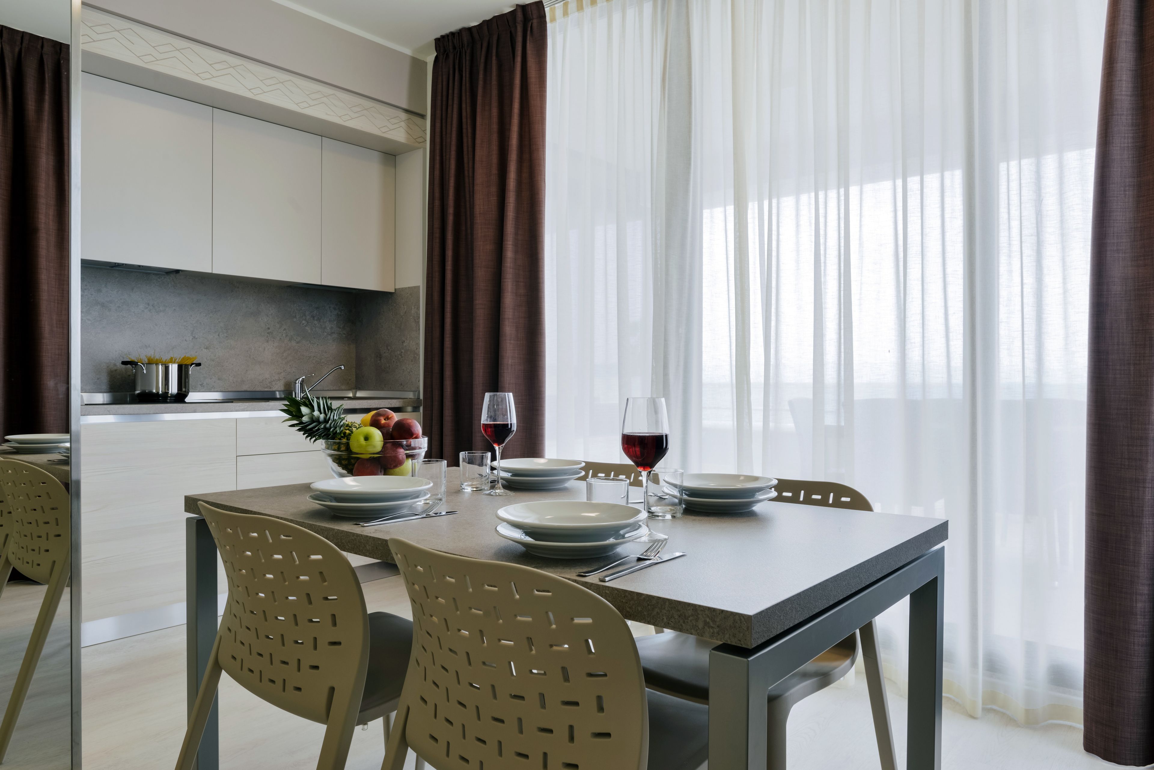 A dining area with a table set for two, a fruit bowl, and wine glasses.