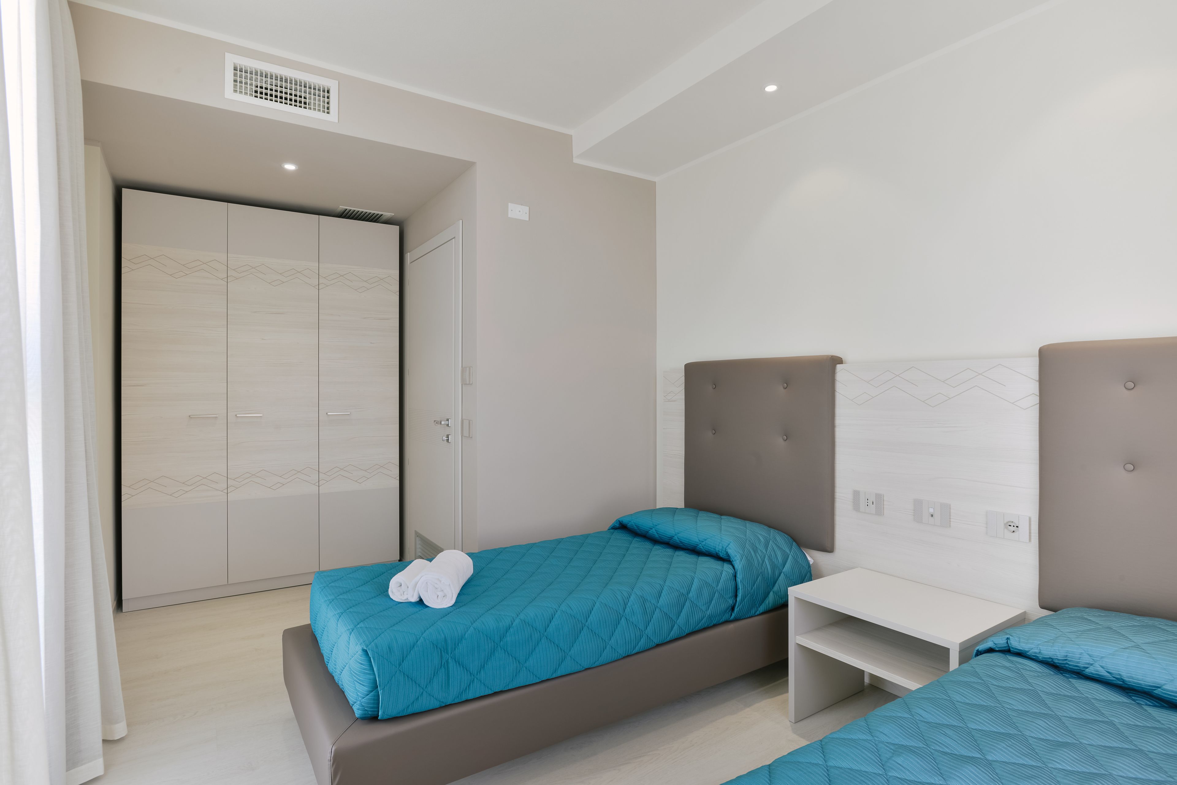 A modern bedroom with two single beds, a bedside table, and a wardrobe.