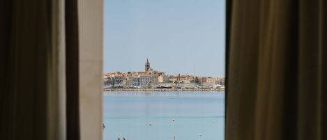 A view of a coastal cityscape through a window with curtains, featuring a prominent church and buildings along the waterfront.