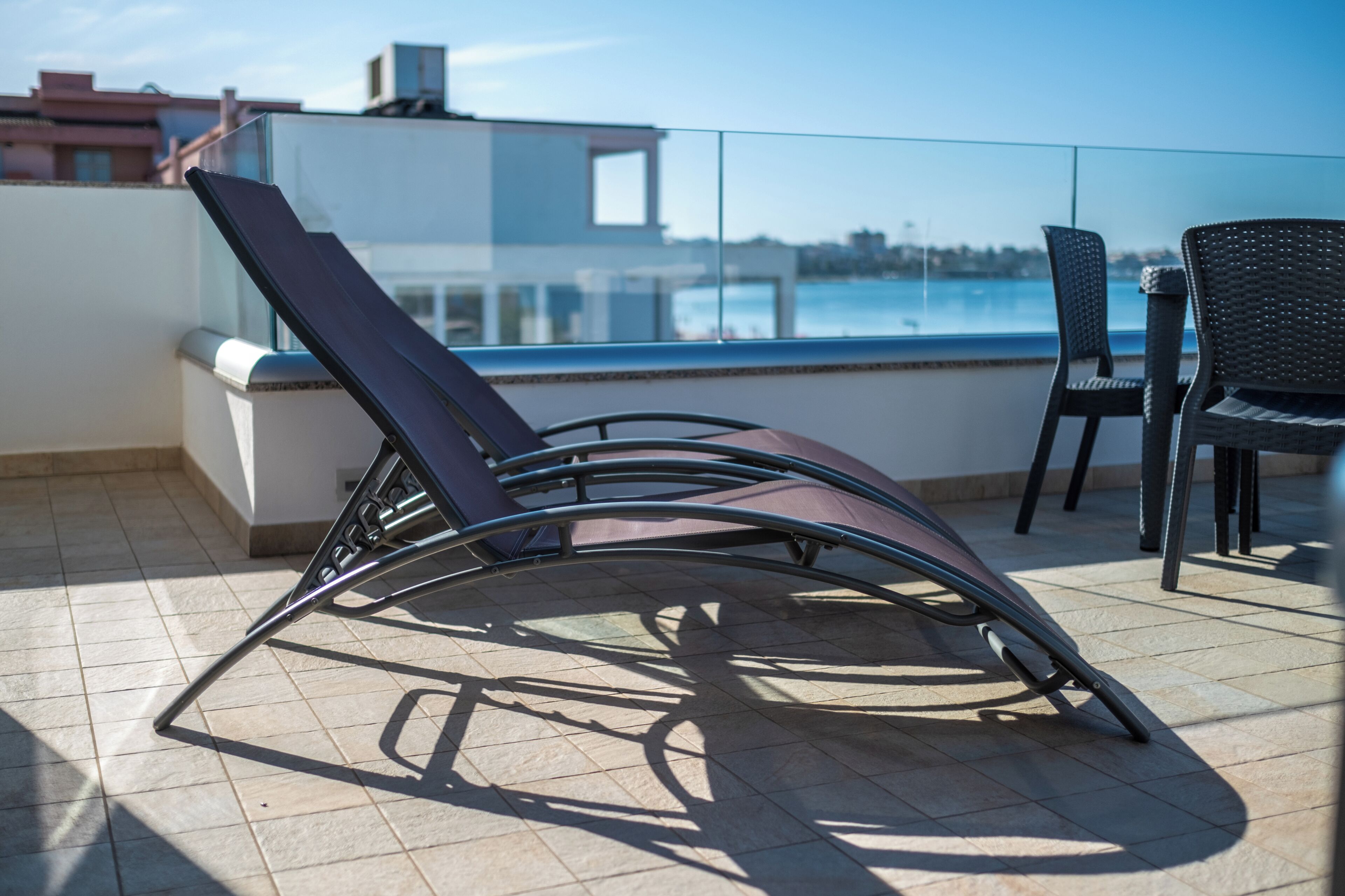 Un balcon avec deux chaises et une table, donnant sur une étendue d’eau et des bâtiments.