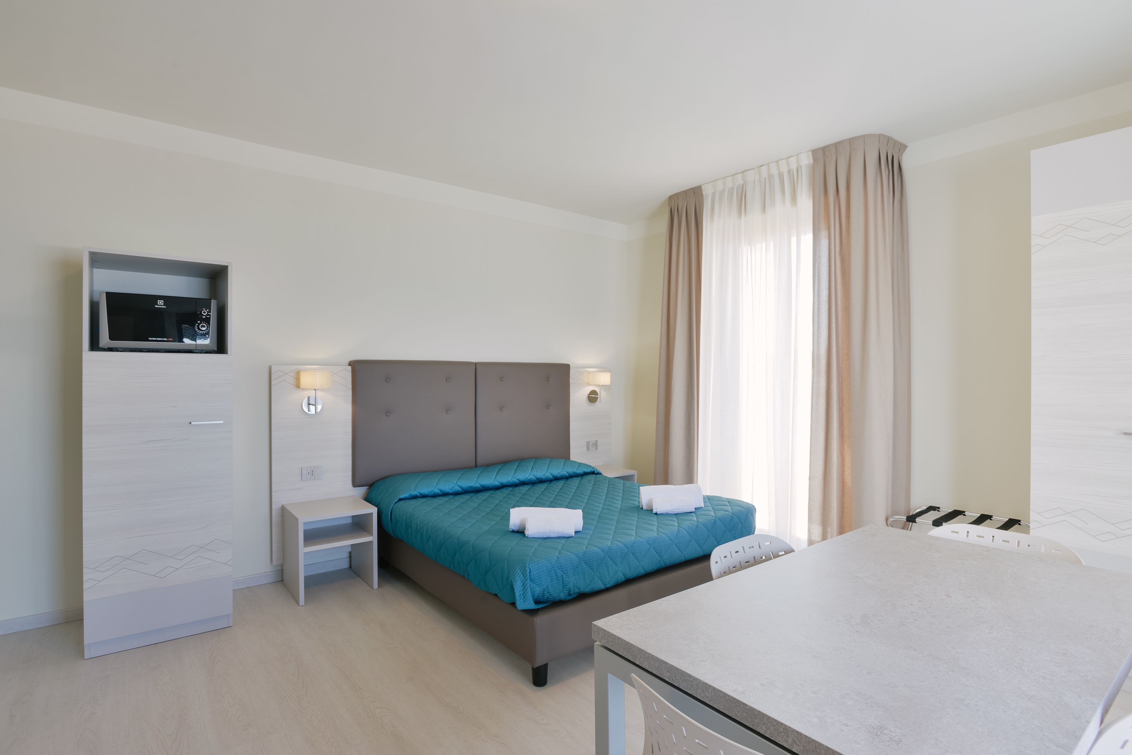 A modern hotel room with a bed, bedside table, and a built-in microwave.